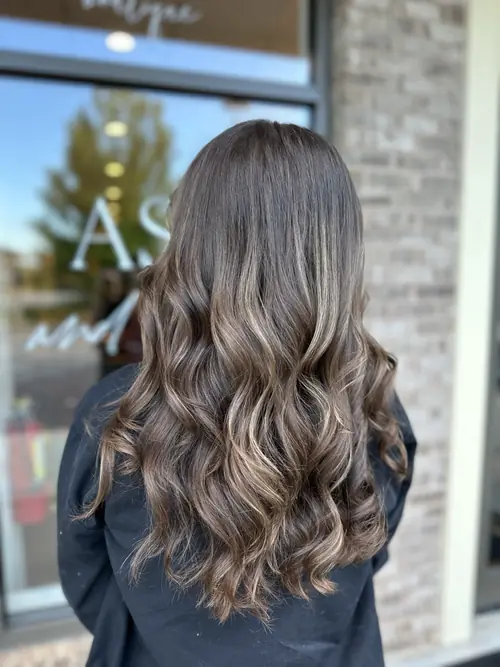 Brunette balayage with warm caramel highlights on long curls, styled at Ash and Ivy Salon in Evans, GA